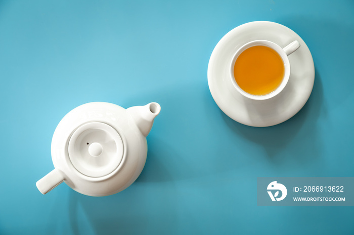 Cup of tea and teapot on a blue background, flat lay.