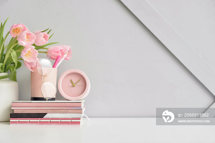 Stylish workplace with notebooks and tulip flowers near light wall