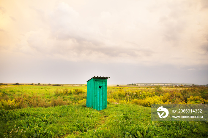 wooden toilet with a carved window in the shape of a heart, an open field.