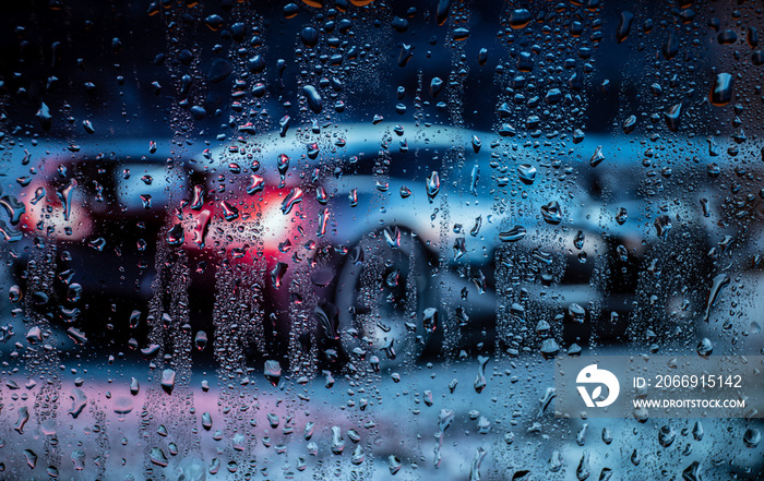 Night city life through windshield. Cars, lights and rain, vintage style photography. City view through a window on a rainy night. Waterdrops on window with road light bokeh.