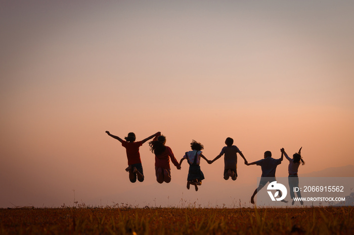 The silhouette of the team of children jumping playing with joy in the mountains in the setting sun