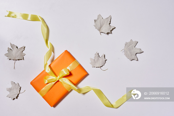 Gift boxes and fall leaves on white background. Creative lay out of autumn leaves and orange present boxes from above. Top view