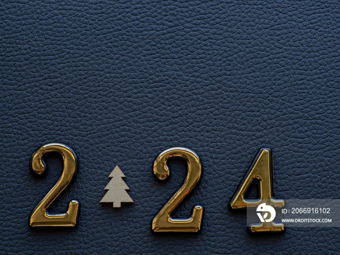 2024 on the dark background. 2024 gold figures lie with small wooden fir tree instead zero on the dark cardboard. Christmas and New year card. Copy space for your text.