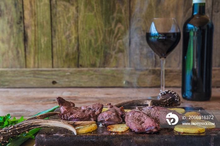 Juste cooked hunter’s meal: smoking roasted deer meat with potatoes and parsley, bottle and glass or red wine