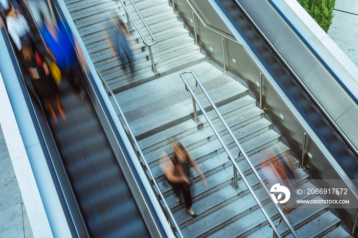 People on stairs and moving escalator at the interchange station near business and commercial center in Paris. Urban scene, city life, public transport hub and traffic concept. Blurred background