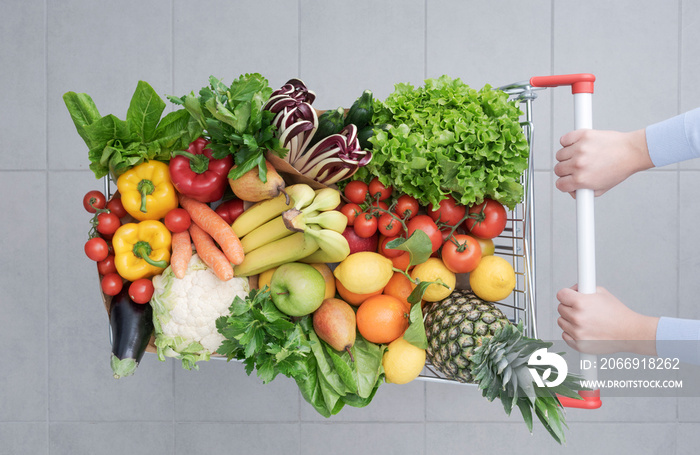 Woman pushing a shopping cart full of vegetables and fruits