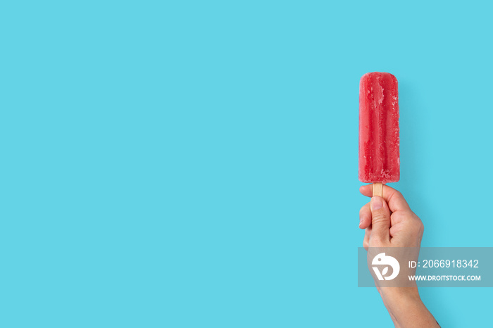 Hand holding a strawberry popsicle on blue background.Copy space