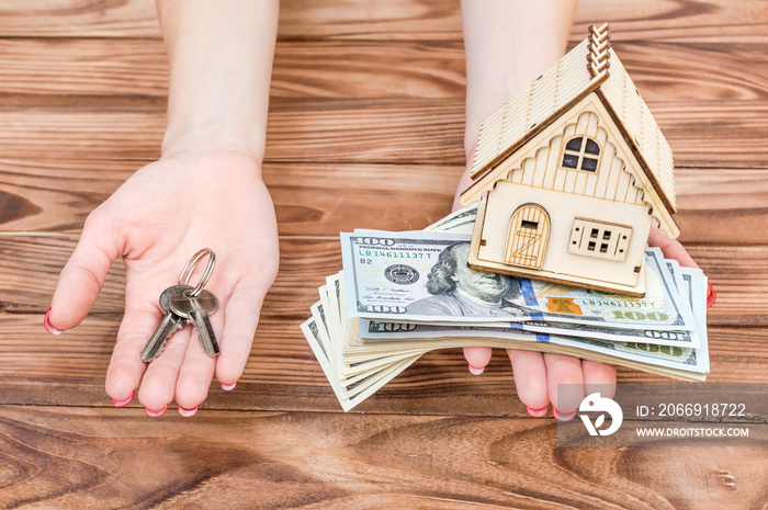 Woman’s hands holding money, model of house and keys of house in palms over wooden table.