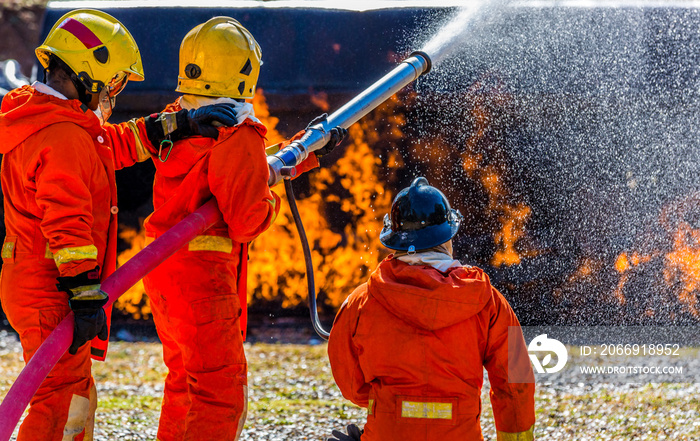 Fireman in helmet and oxygen mask spraying water to fire surround with smoke and drizzle, Firefighter in fire fighting operation, Firefighter using extinguisher and water from hose for fire fighting.