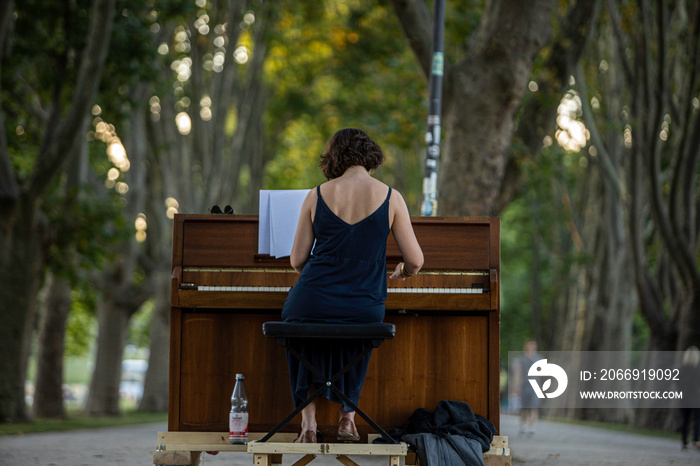 Street artist woman playing piano in German park, Cologne city.