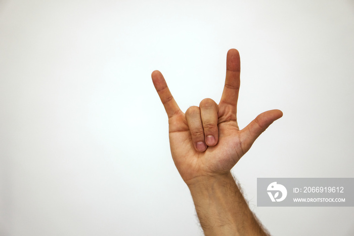 A hand on a white background shows a rock and roll gesture. The Caucasian man raised his hand in the air . High quality photo