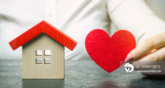 A woman holds a red heart near the wooden house. Insurance agent services. Property insurance concept. Protection of housing. Security and safety family and life. Protect the home. Support