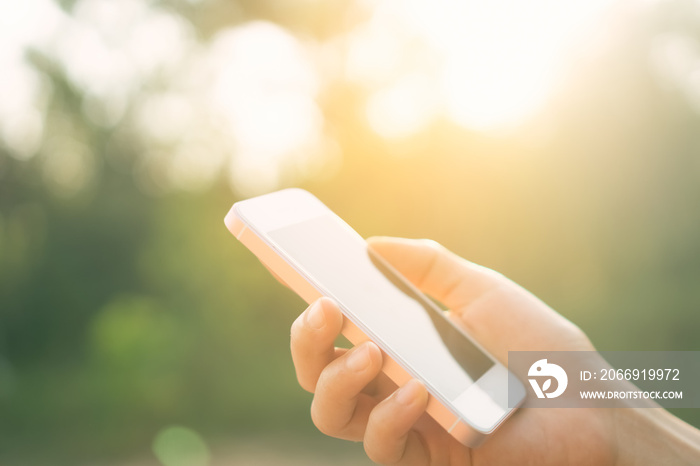 Woman hand using smart phone at outdoor nature park with sunset sky abstract background.