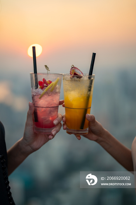 Beautiful Asian woman friends meeting and drinking cocktail together at skyscraper rooftop restaurant in metropolis at summer sunset. Female friend enjoy outdoor lifestyle activity in the city at nigh