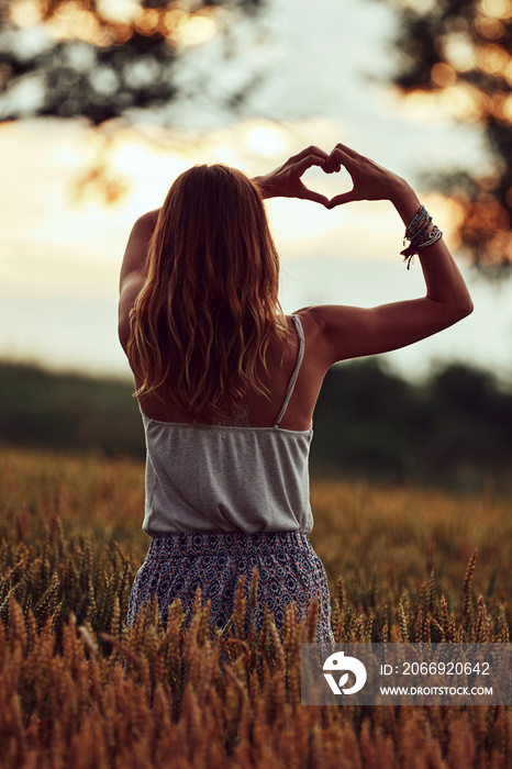 Woman in nature holding heart-shape symbol made with hands.