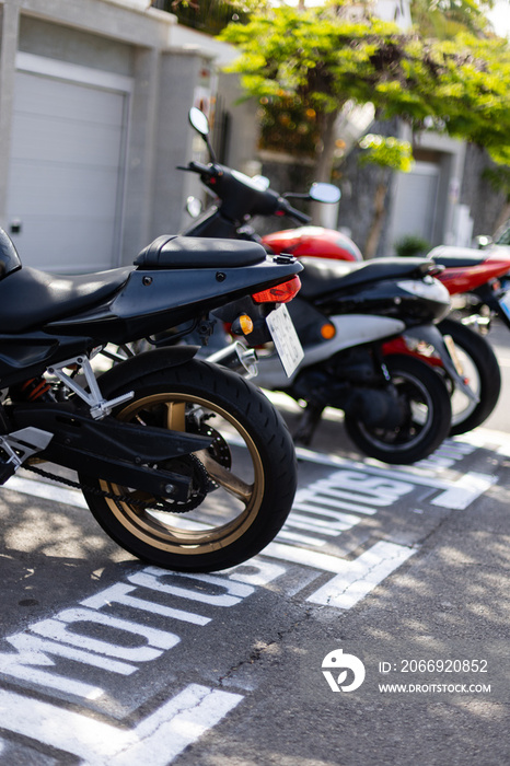 Motorbikes parked on a parking lot outside near houses. Sign on the road.