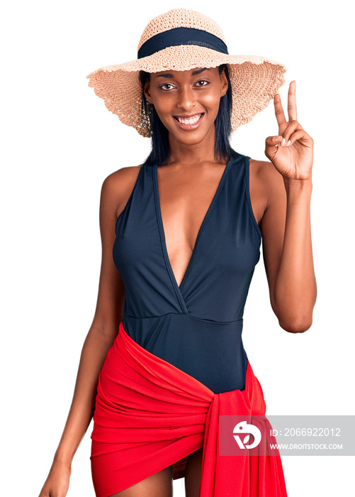 Young african american woman wearing swimsuit and summer hat showing and pointing up with fingers number two while smiling confident and happy.