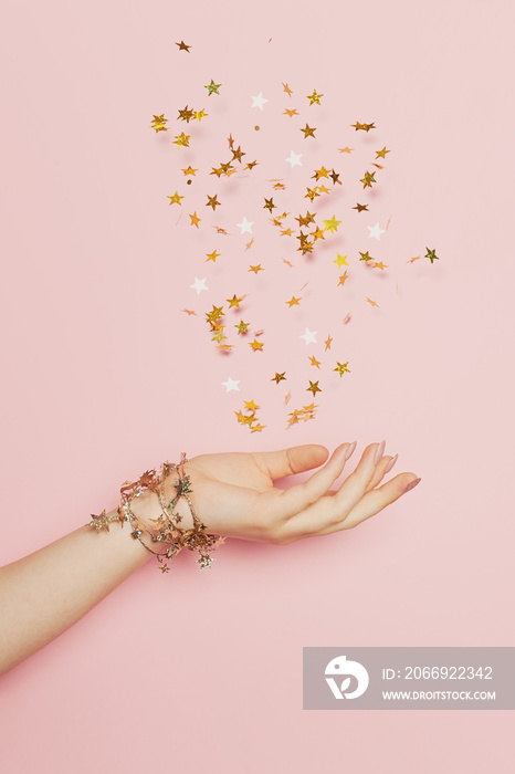 Celebration, wedding and birthday party concept. Gold confetti stars blowing up in female hand on pastel pink background