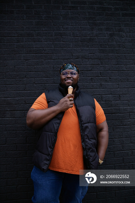 Happy plus-sized guy enjoying ice cream in front of black wall