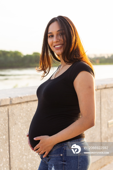 Portrait of hispanic pregnant woman walking in a park at sunset. Pregnancy and motherhood concept.