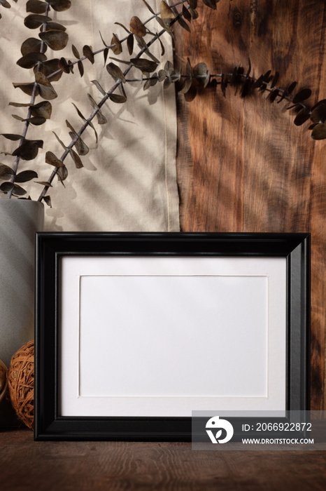 blank black photo frame with kitchenware on wood table with sunlight