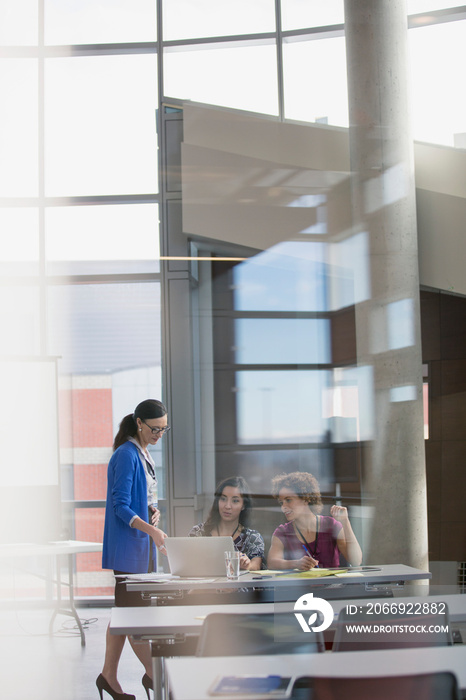 View through glass wall of woman helping conference attendees.