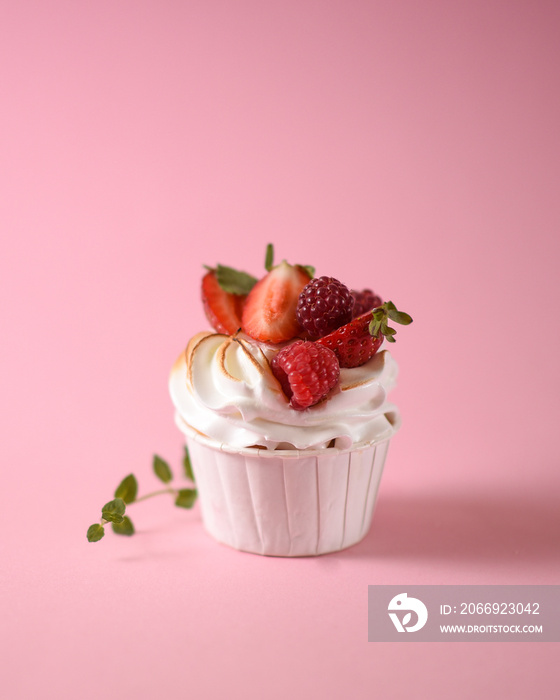 Cupcake with meringue and raspberry candy. homemade cakes isolated on pink background. Side view of a cupcake garnished with fresh strawberries