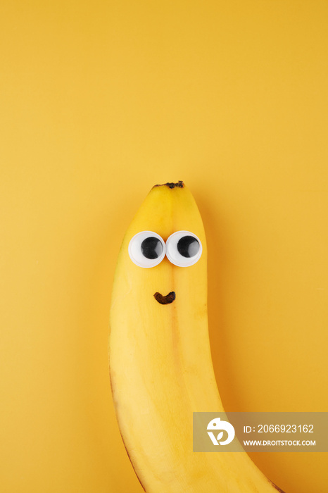 Funny smiling banana with eyes concept isolated on yellow background with copy space