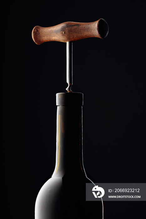 Bottle of red wine with corkscrew on a black background.