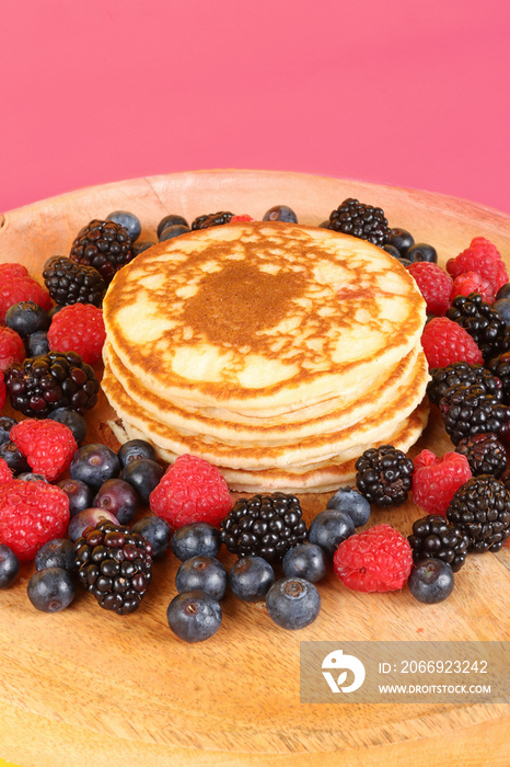 Pancakes with red fruits: blueberries, raspberries and blackberries on a colorful  background