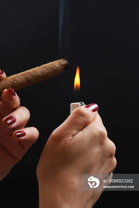 lighter with a spark and a cigar in female hands on a black background