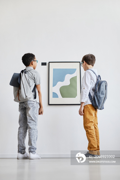 Minimal full length portrait of two schoolboys looking at abstract paintings in modern art gallery, copy space