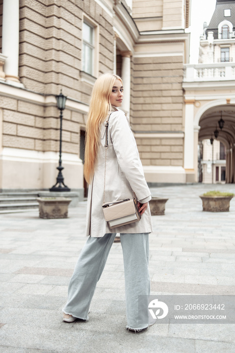 Portrait of young fashion blonde woman in autumn trench coat against the background of urban architecture