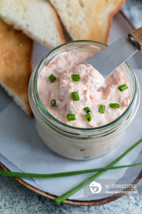 Salmon and soft creme cheese spread in jar. Salmon rillettes, mousse, pate and toasts on gray background