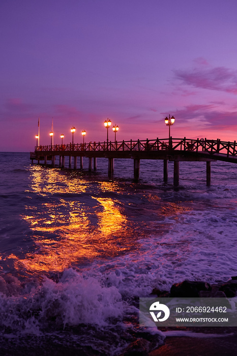 Long pier on the sea in Marbella, Costa del Sol, Spain. Illuminated wooden jetty on a beach in Marbella during sunset. Pier of marbella. Coastal pier into the Mediterranean sea in Marbella, Spain.