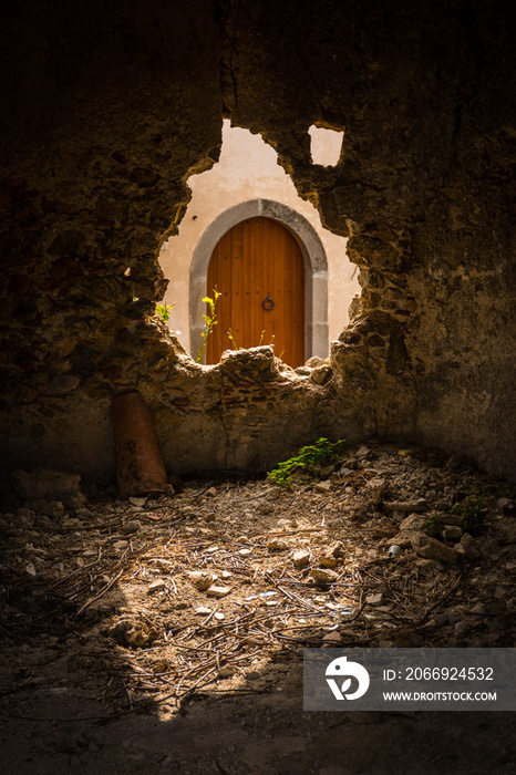 An old wooden arched door in Sicily seen through a broken hole in a stone wall