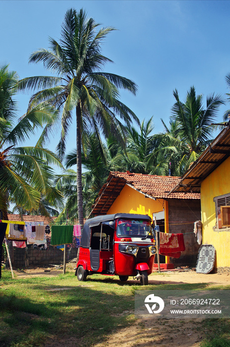 Tuk tuk taxi in Sri Lanka. Typical vehicle parked in the garden. Red tuk-tuk car.