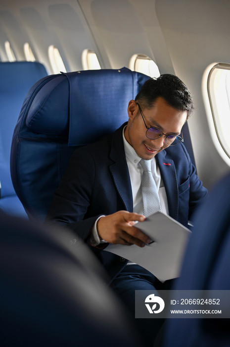 Businessman in formal suit reading business paperwork during the flight to his destination.