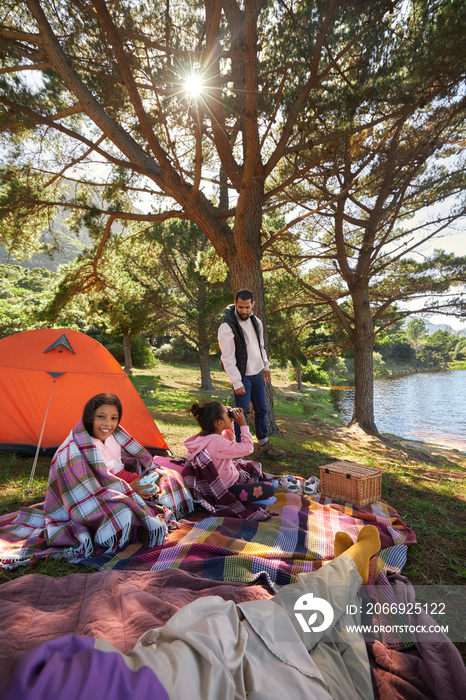 Young family cozy up by the tent during camping trip with lake and nature backdrop