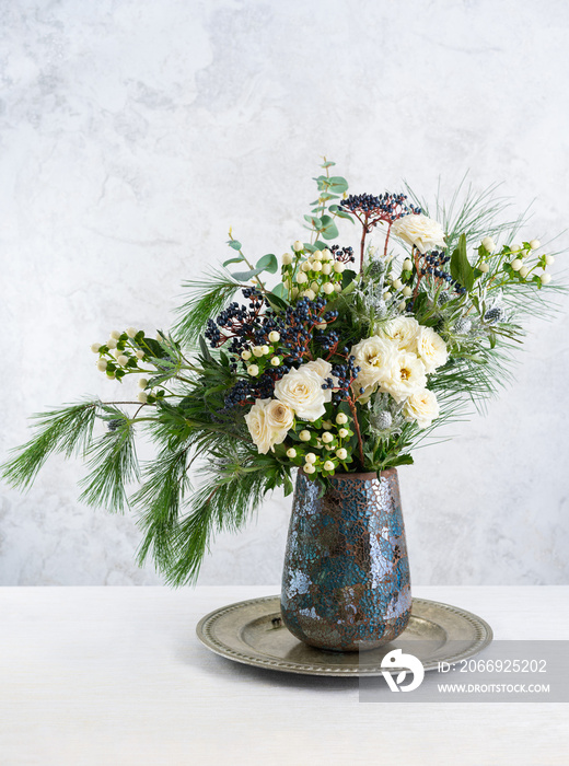 Beautiful winter bouquet in vase. Flower arrangement with roses, fir branches, winter berries, eucalyptus and eryngium. Christmas flower decoration.