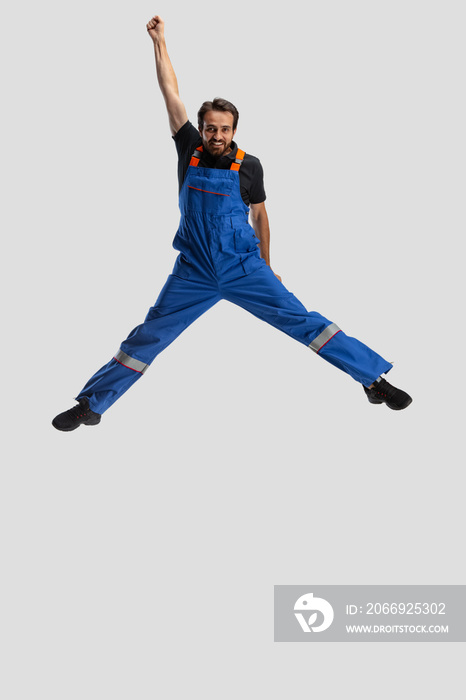 Comic portrait of young man, male auto mechanic in dungarees jumping, flying up isolated over white studio background. Concept of occupation, funny meme emotions