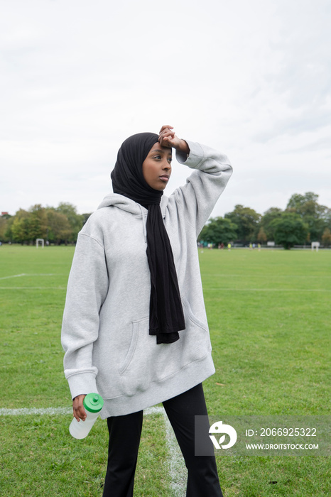 Portrait of woman in hijab standing in soccer field with water bottle