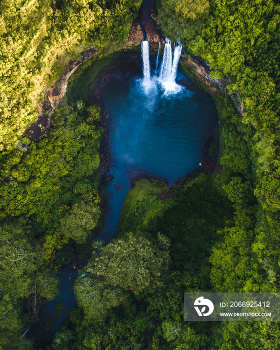 Magical Hawaiian waterfall surrounded by trees at sunrise, beautiful golden light and lush green forests