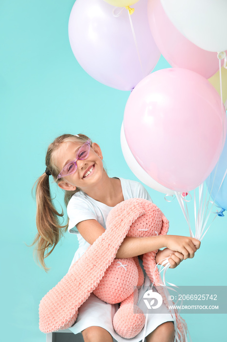 Little girl with balloons and toy bunny on color background