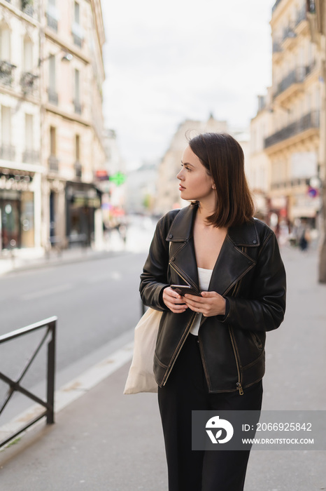 young woman in black jacket holding smartphone on street in paris.