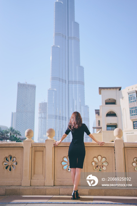 Beautiful young woman in black dress and long hair enjoying Dubai Downtown view.