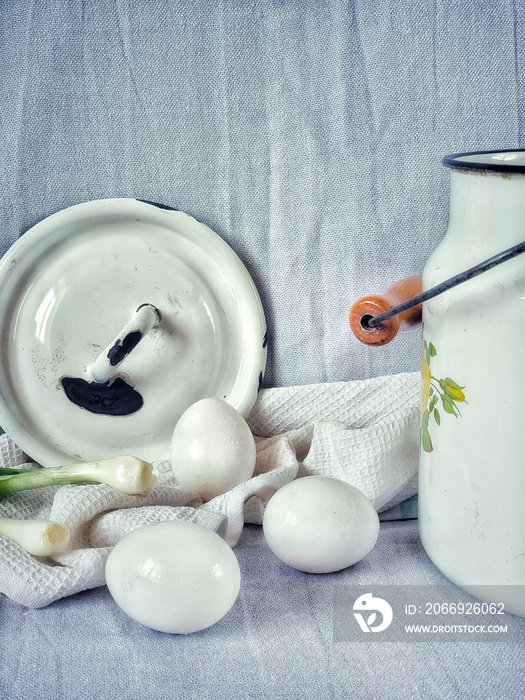 rustic still life with eggs, milk can and green onions on a white background