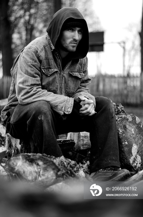 Homeless, sad man in a beanie sitting outside and feeling cold, trying to warm up his hands