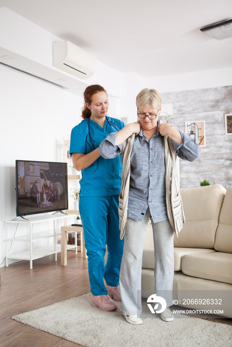 Young female nurse helping senior woman to get dressed