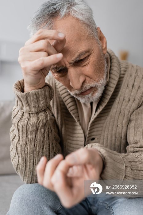 worried man with parkinsonian syndrome looking at trembling hand on blurred foreground.